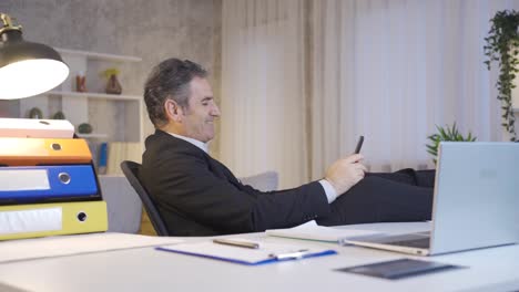 Mature-businessman-working-in-home-office-looking-at-phone-with-happy-and-smiling.